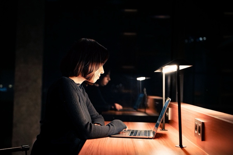 A practice owner working late at her desk, lamp on, laptop open
